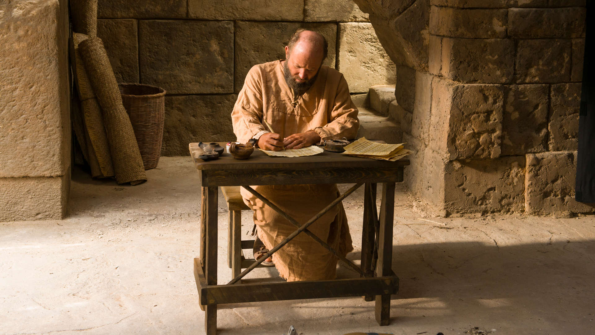 A still from a Bible Video of Paul writing an epistle on a piece of paper on a desk