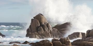 Waves break on rocks on a shore.